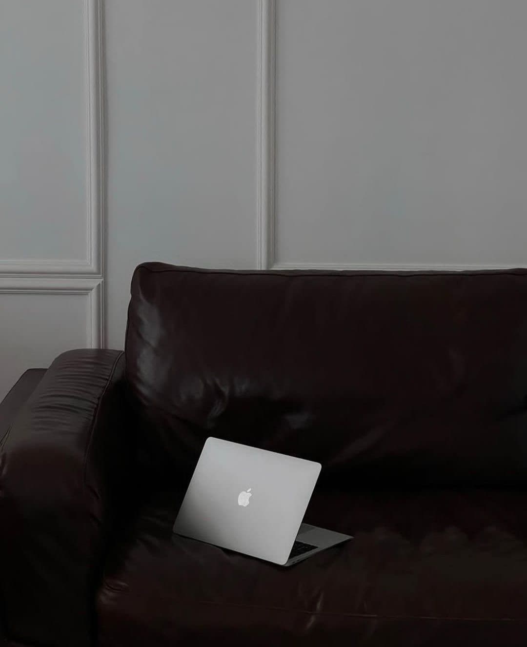 Portátil sobre un sofá de piel oscuro junto a una pared con molduras